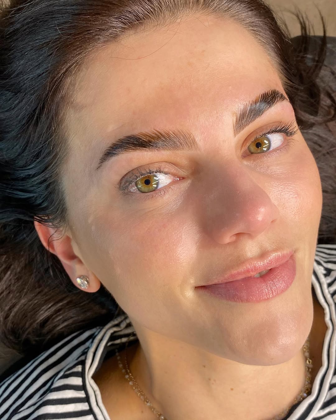 Smiling person lying down, wearing a striped shirt and a small earring, with natural makeup.