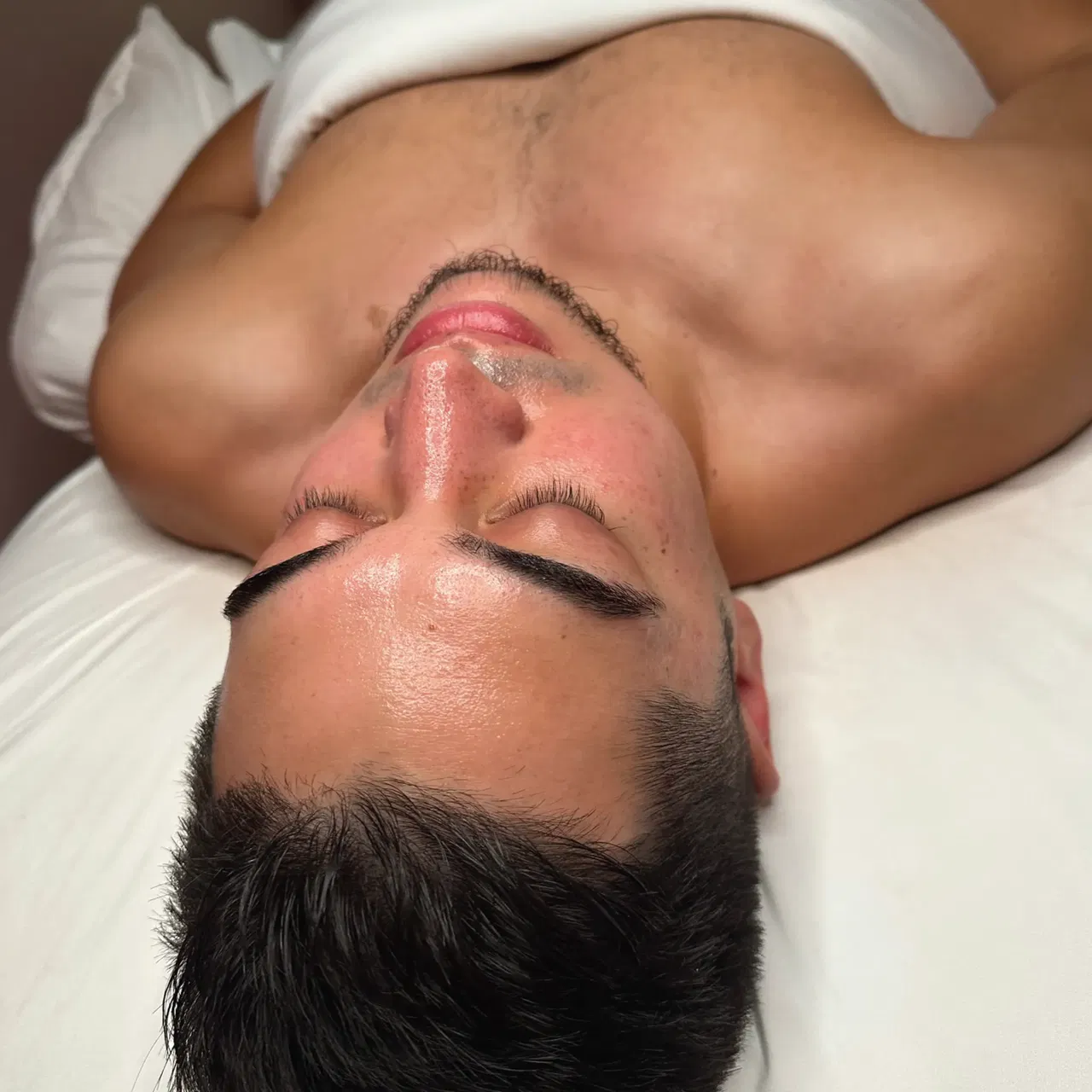 Man lying on back, eyes closed, with towel draped over shoulders, showing relaxed expression.