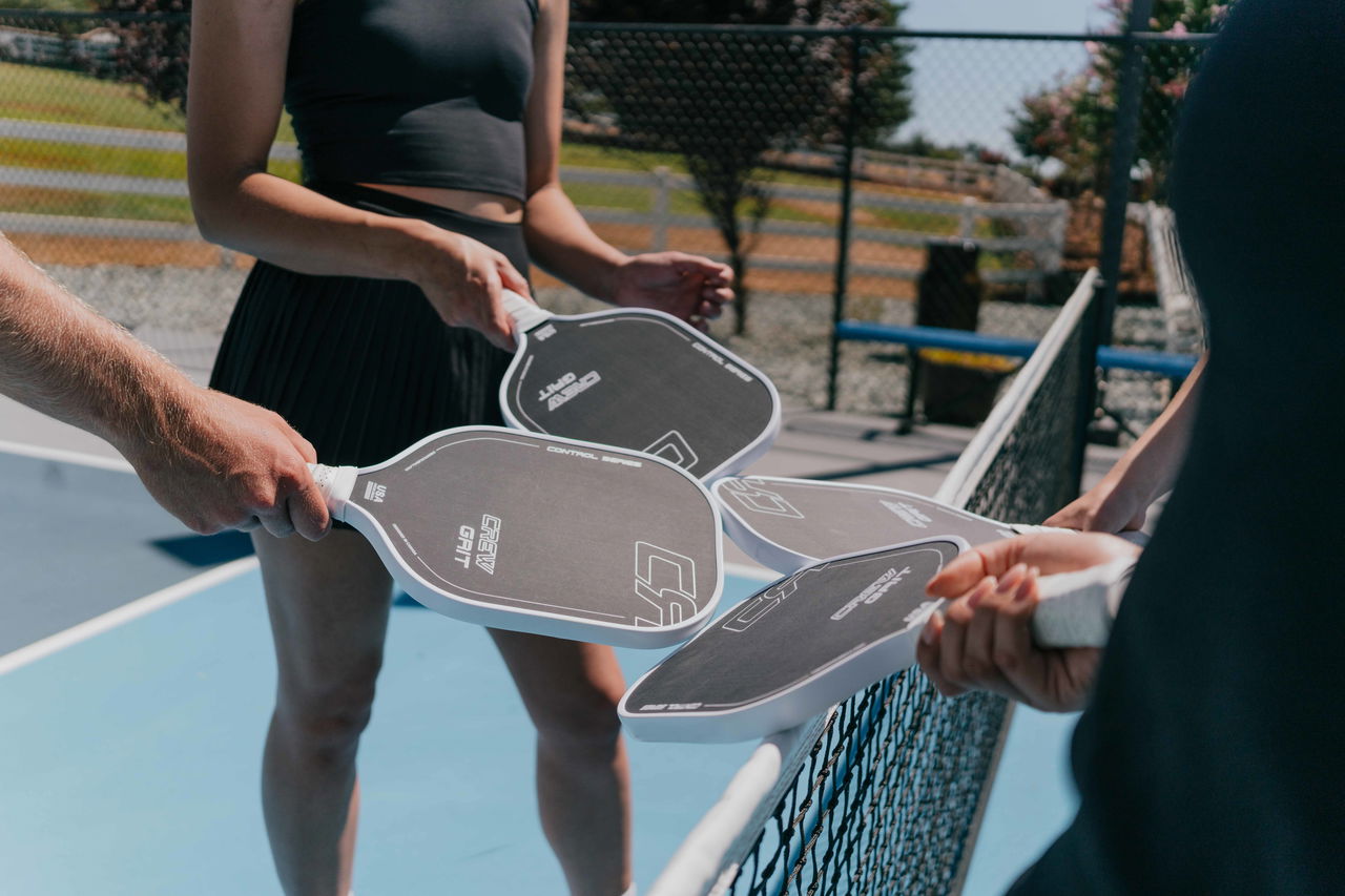 Four people holding pickleball paddles over a net on an outdoor court.