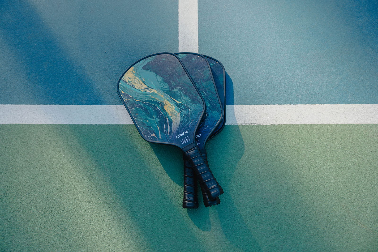 Two pickleball paddles with abstract designs resting on a court's blue and green surface.