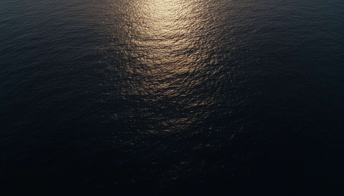 Aerial view of deep dark ocean water with golden sunlight glinting on the ripples