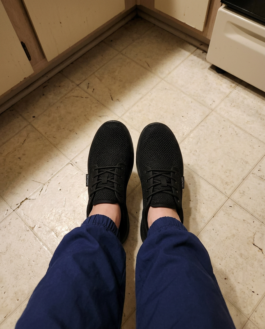 Looking down at feet wearing black knit wide toe box sneakers on a kitchen floor