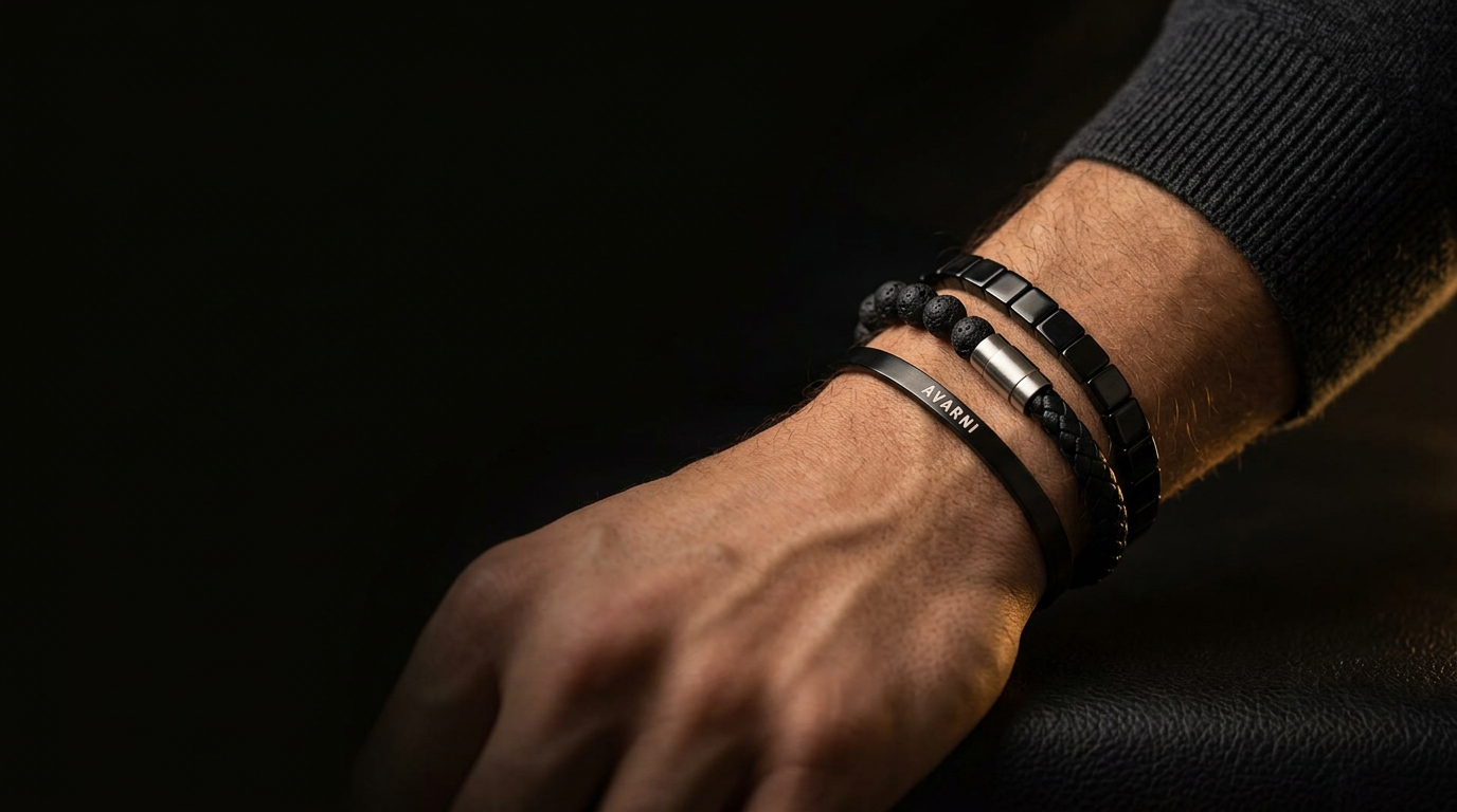 Man's wrist wearing a stack of Avarni bracelets: black cuff, lava stone beads, braided leather and black link bracelet
